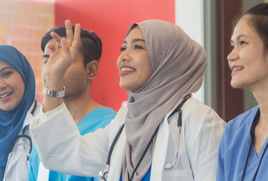 Hijabi doctor smiling and raising her hand
