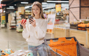 Customer using smartphone and choosing pomegranate in supermarket
