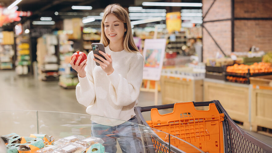 Customer using smartphone and choosing pomegranate in supermarket