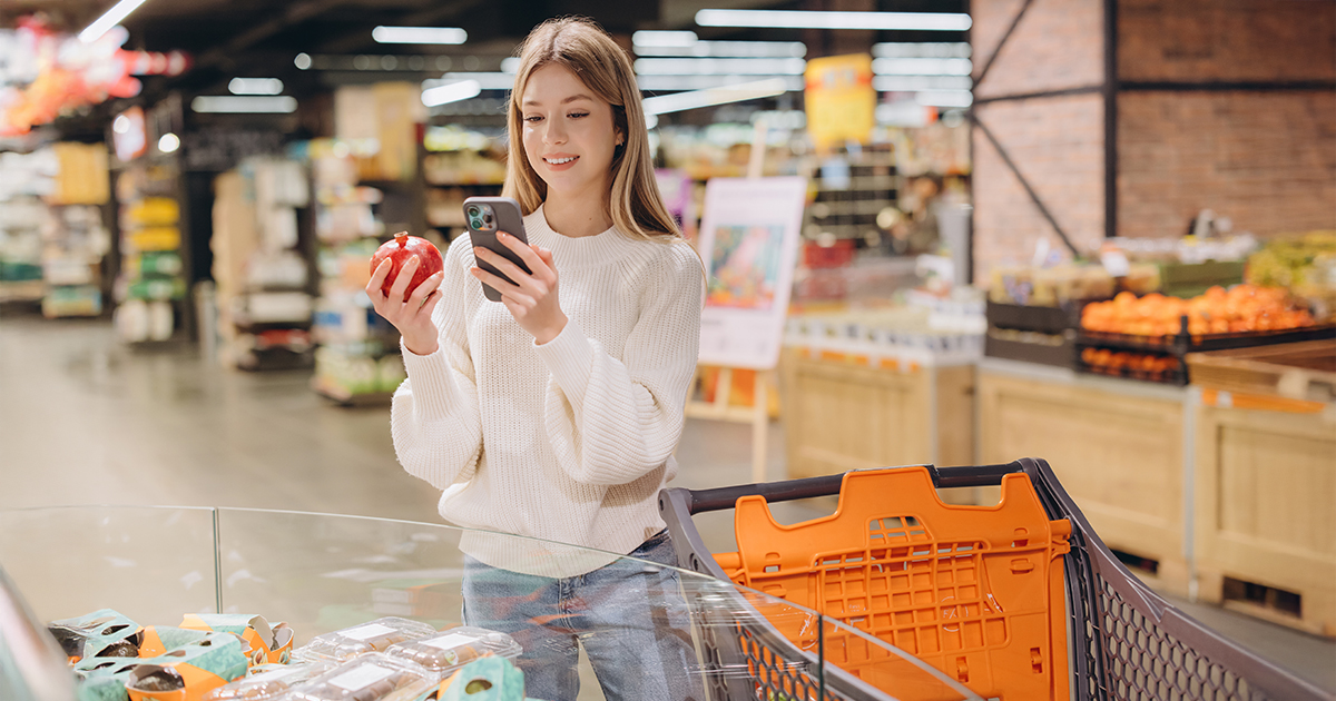 Customer using smartphone and choosing pomegranate in supermarket