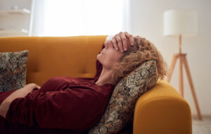 Woman with sinus pain, headache and stomach problems, lying on a couch at home
