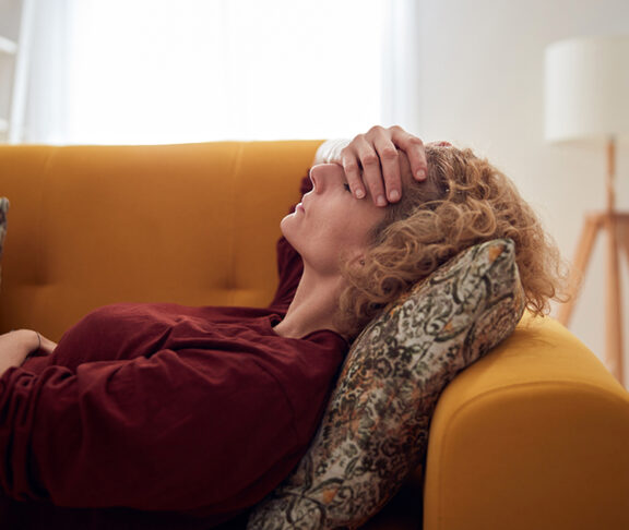 Woman with sinus pain, headache and stomach problems, lying on a couch at home
