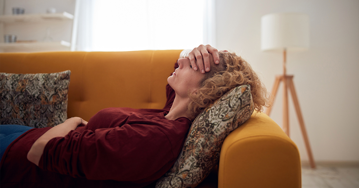Woman with sinus pain, headache and stomach problems, lying on a couch at home