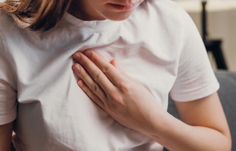 Young unhealthy female sit on couch having difficulty breathing pain of heart, touches his chest with hand