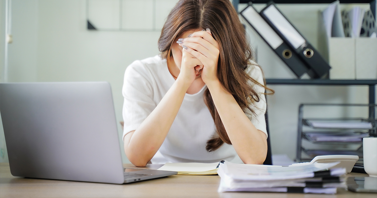 A woman is sitting at a desk with a laptop and a stack of papers