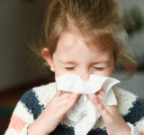 little girl blowing her nose and covering it with handkerchief with eyes closed