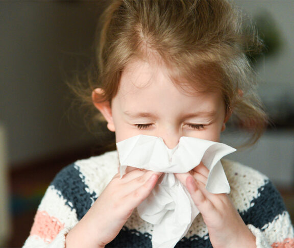 little girl blowing her nose and covering it with handkerchief with eyes closed