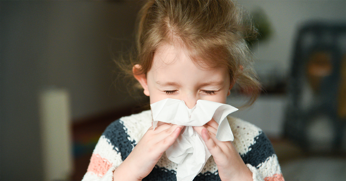 little girl blowing her nose and covering it with handkerchief with eyes closed