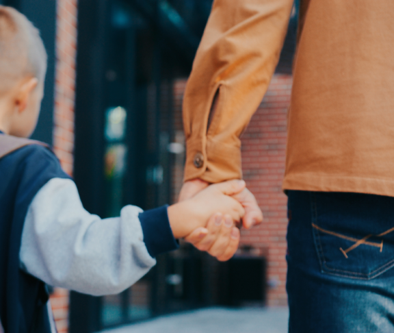 Blick von hinten auf den kleinen kaukasischen Jungen, der mit seinem fürsorglichen Vater zusammen geht. Vater, der den kleinen Jungen in der Schule abgesetzt hat. Er hält seine Hand. Rucksack mit Büchern. Moderne Schule.
