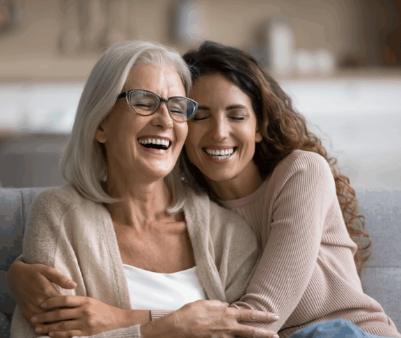 Fröhlich aufgeregt Mutter und erwachsene Tochter Frau, die sich zu Hause amüsiert, mit Kopf berühren, auf dem Sofa sitzen, mit geschlossenen Augen lachen, lustiges Gespräch genießen, Freizeit, Familienaffektion