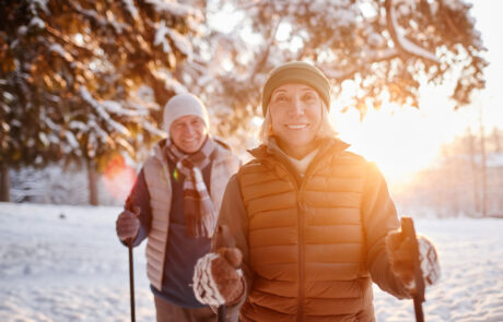 Waist up portrait of smiling mature couple enjoying Nordic walk in winter forest at sunset