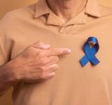 Detailhände eines älteren Mannes, der ein blaues Band auf beigem Studiohintergrund zeigt. Prostatakrebs, Bewusstseinskonzept.