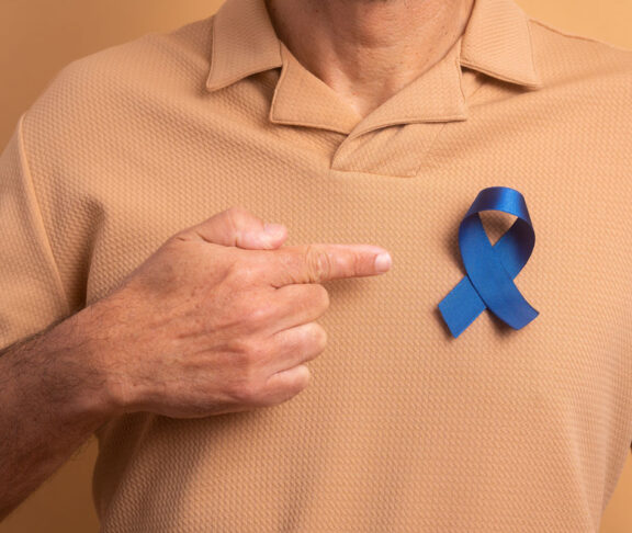 Detailhände eines älteren Mannes, der ein blaues Band auf beigem Studiohintergrund zeigt. Prostatakrebs, Bewusstseinskonzept.