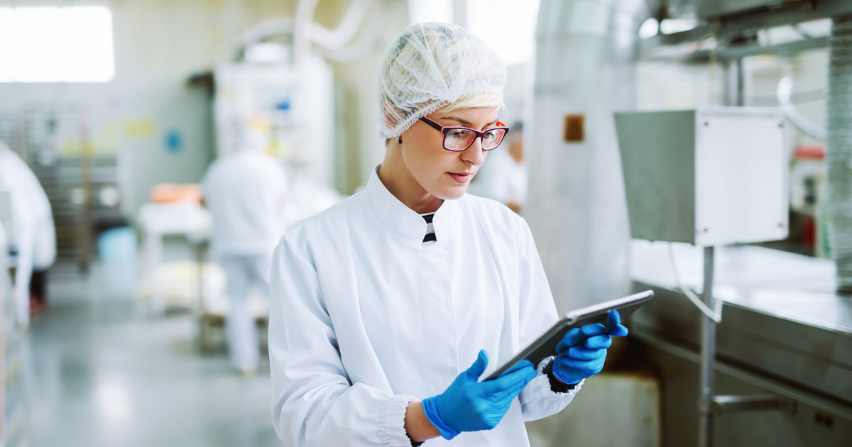 Female worker using tablet for controling products while standing in factory.