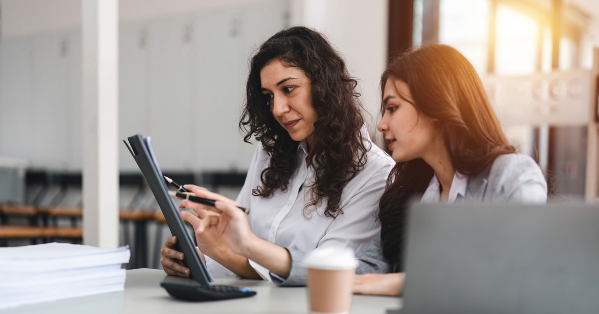 Two smart multiethnic business people working together with laptop while working on project in office