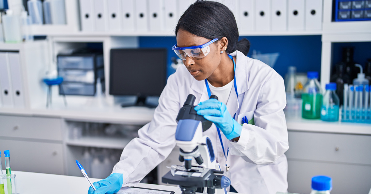 Young african american woman scientist using microscope write on document at laboratory