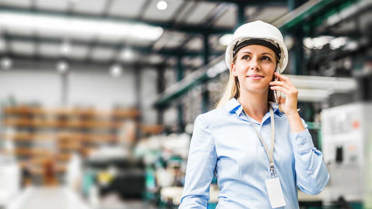 A portrait of an industrial woman engineer standing in a factory, making a phone call.