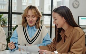 Candid shot of two smiling young women reading documents while enjoying work meeting in office and discussing business