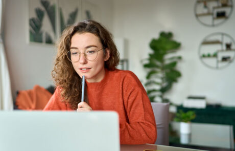 Young girl female student using laptop elearning or remote working at home office looking at computer watching webinar, learning training, studying online seminar or video calling for work meeting.