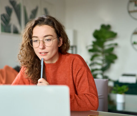 Young girl female student using laptop elearning or remote working at home office looking at computer watching webinar, learning training, studying online seminar or video calling for work meeting.