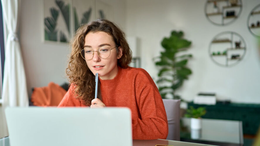 Young girl female student using laptop elearning or remote working at home office looking at computer watching webinar, learning training, studying online seminar or video calling for work meeting.