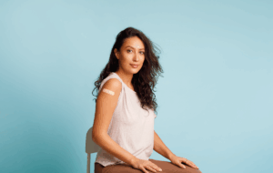 Stoppen Sie Coronavirus, Impfkampagne. Geimpfte Frauen, die einen Arm zeigen und sich mit den nach HPV-Impfung aufrollenden Blättern auf blauem Hintergrund positionieren. Studioaufnahme