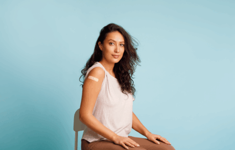 Stoppen Sie Coronavirus, Impfkampagne. Geimpfte Frauen, die einen Arm zeigen und sich mit den nach HPV-Impfung aufrollenden Blättern auf blauem Hintergrund positionieren. Studioaufnahme