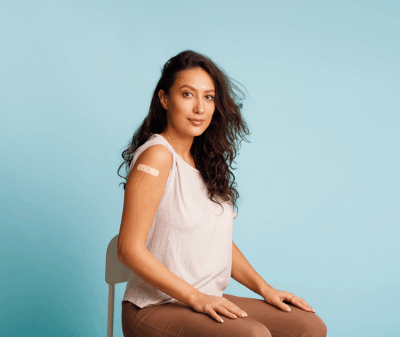 Stoppen Sie Coronavirus, Impfkampagne. Geimpfte Frauen, die einen Arm zeigen und sich mit den nach HPV-Impfung aufrollenden Blättern auf blauem Hintergrund positionieren. Studioaufnahme