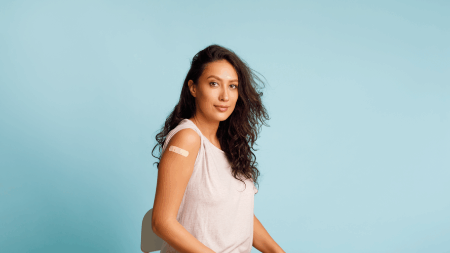 Stoppen Sie Coronavirus, Impfkampagne. Geimpfte Frauen, die einen Arm zeigen und sich mit den nach HPV-Impfung aufrollenden Blättern auf blauem Hintergrund positionieren. Studioaufnahme