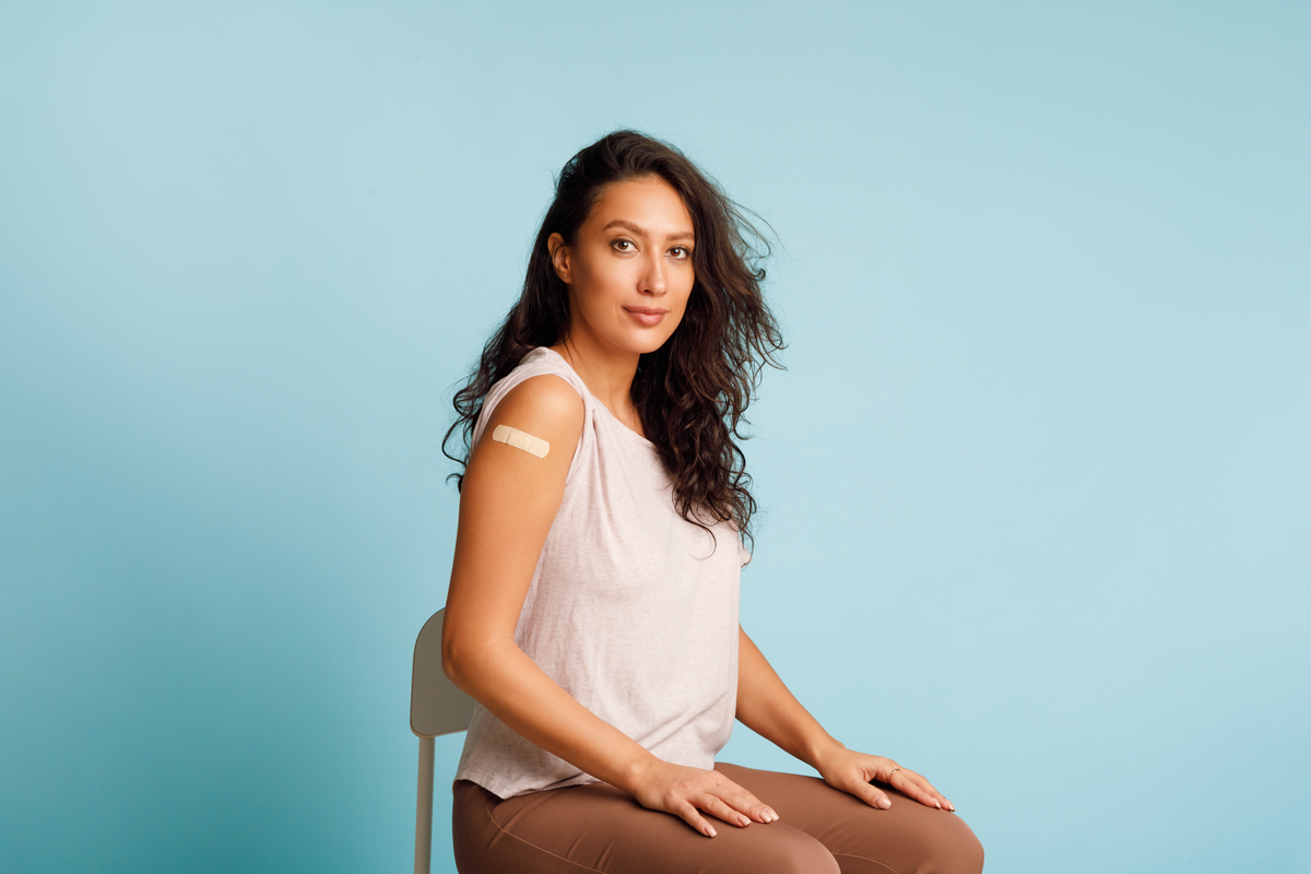 Stoppen Sie Coronavirus, Impfkampagne. Geimpfte Frauen, die einen Arm zeigen und sich mit den nach HPV-Impfung aufrollenden Blättern auf blauem Hintergrund positionieren. Studioaufnahme