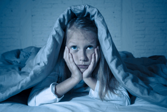 Das süße kleine, kaukasische Mädchen, das im Bett liegt und mit einer Decke bedeckt ist, die sich erschöpft und schlaflos an Schlaflosigkeit Depression Leid in Kinder Emotionale und Schlafstörungen Konzept.