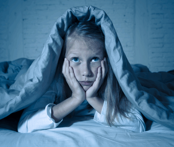 Das süße kleine, kaukasische Mädchen, das im Bett liegt und mit einer Decke bedeckt ist, die sich erschöpft und schlaflos an Schlaflosigkeit Depression Leid in Kinder Emotionale und Schlafstörungen Konzept.