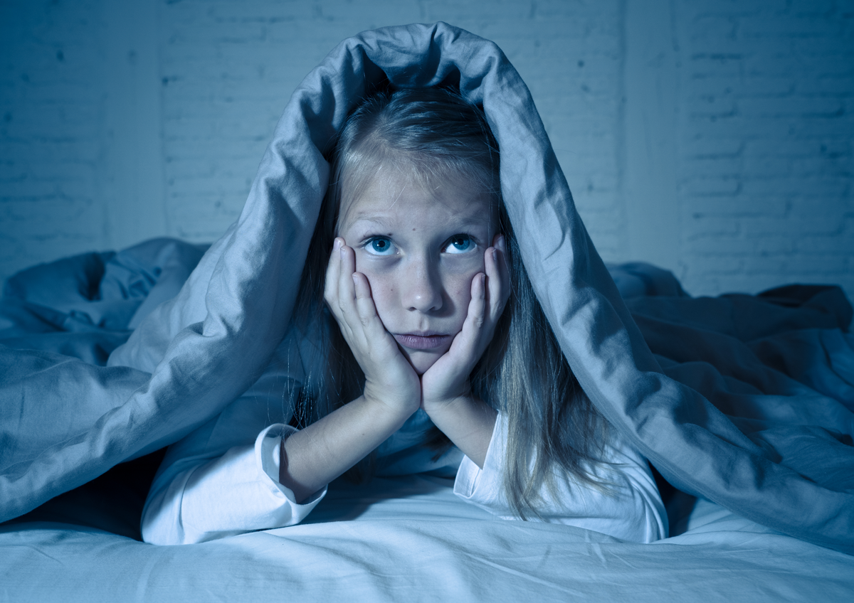 Das süße kleine, kaukasische Mädchen, das im Bett liegt und mit einer Decke bedeckt ist, die sich erschöpft und schlaflos an Schlaflosigkeit Depression Leid in Kinder Emotionale und Schlafstörungen Konzept.