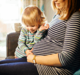 Pregnant mother sitting on sofa with child
