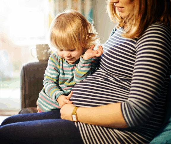Pregnant mother sitting on sofa with child
