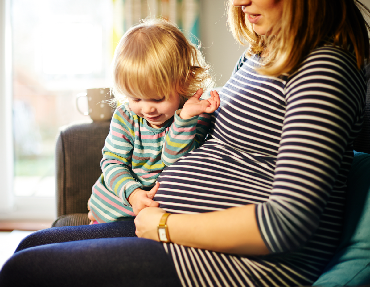 Pregnant mother sitting on sofa with child