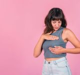 Frau, die eine Brust-Selbstprüfung auf rosafarbenem Hintergrund durchführt. Leerzeichen kopieren