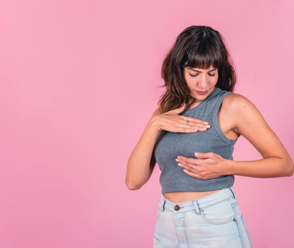 Frau, die eine Brust-Selbstprüfung auf rosafarbenem Hintergrund durchführt. Leerzeichen kopieren