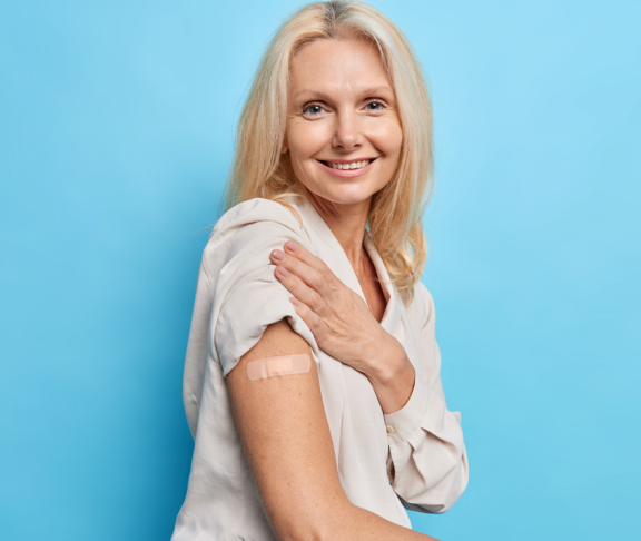 Sideways Aufnahme von blonde vierzig Jahre alte Frau genehmigt Impfkampagne erhält Inokulation von covid 19 Virus fühlt sich geschützt einzeln auf blauem Hintergrund. Geimpfte Europäerin mittleren Alters