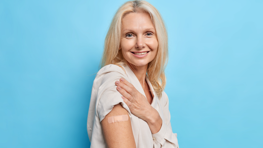 Sideways Aufnahme von blonde vierzig Jahre alte Frau genehmigt Impfkampagne erhält Inokulation von covid 19 Virus fühlt sich geschützt einzeln auf blauem Hintergrund. Geimpfte Europäerin mittleren Alters