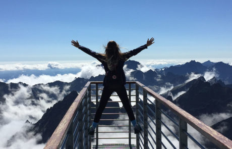 kvinne med ryggen til som står på en bro med fjell utsikt