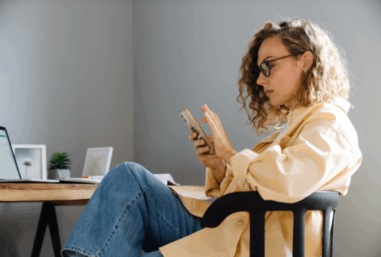 Junge, schwul-ernste Frau in Brillen mit Telefon, das im gemütlichen Zimmer zu Hause sitzt