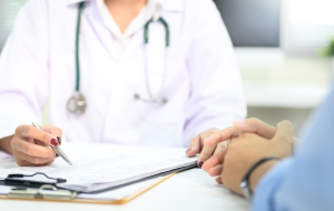 Nahaufnahme der ärztlichen Beratung mit dem Patienten, Hinweis auf medizinische Dokumente während der Untersuchung.