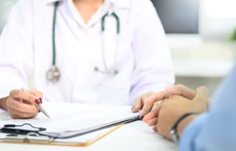 Nahaufnahme der ärztlichen Beratung mit dem Patienten, Hinweis auf medizinische Dokumente während der Untersuchung.