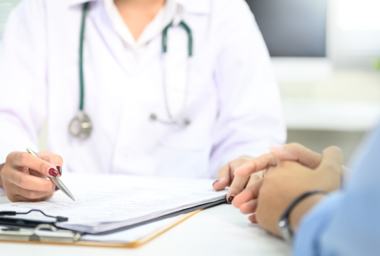 Nahaufnahme der ärztlichen Beratung mit dem Patienten, Hinweis auf medizinische Dokumente während der Untersuchung.