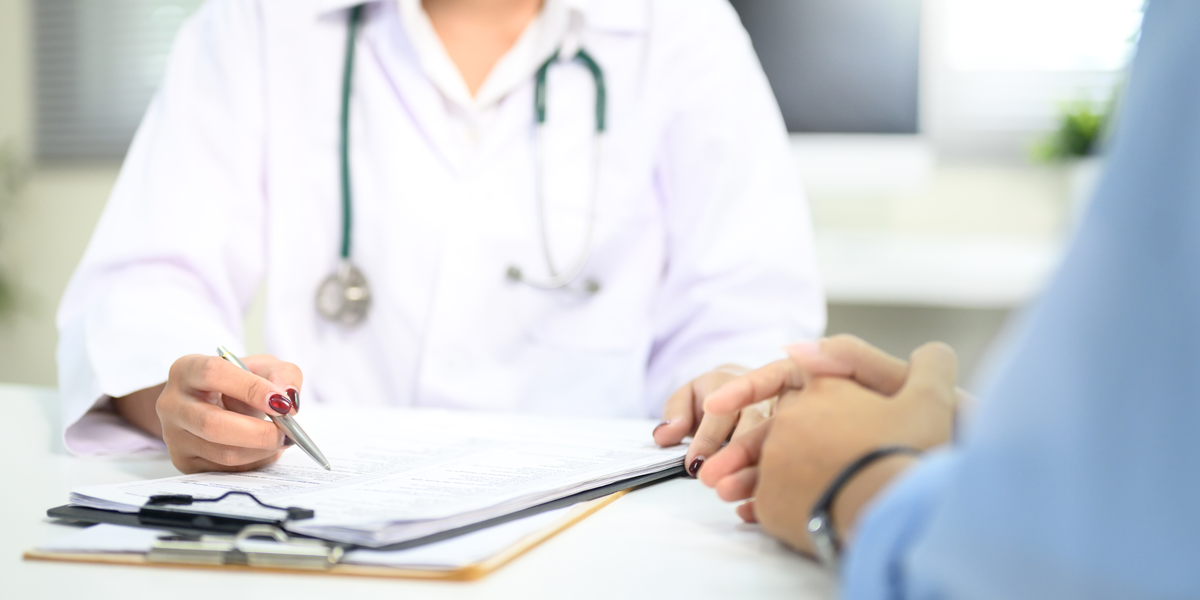 Nahaufnahme der ärztlichen Beratung mit dem Patienten, Hinweis auf medizinische Dokumente während der Untersuchung.