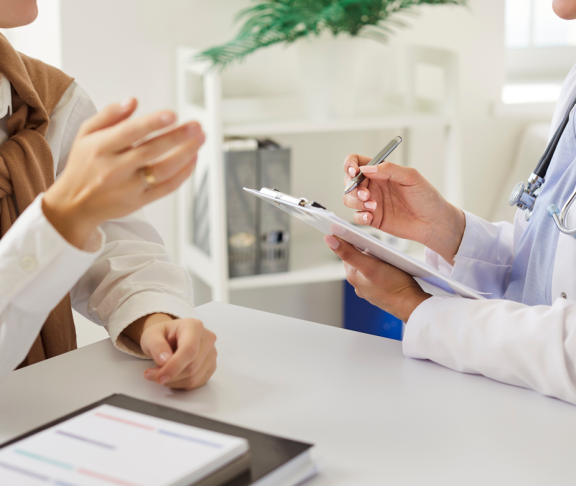 Zugeschnittene Ansicht des weiblichen Arztes aufmerksam zuhören Frau Patientin und Notizen während der Beratung. Arzt oder Kardiologe, der sich auf das Verständnis und die Behandlung von Fragen der Patientengesundheit konzentriert.