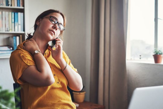 Cropped shot of an attractive young businesswoman sitting alone in her home office and feeling stressed while using her cellphone