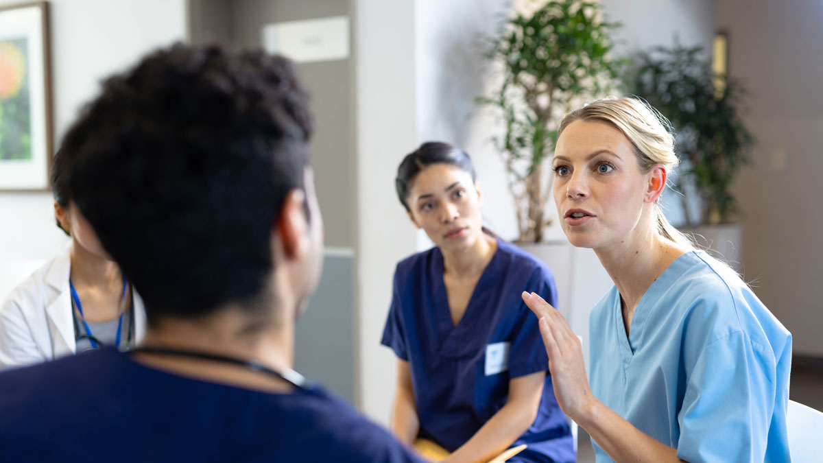 Caucasian female doctor sitting talking with diverse colleagues at hospital