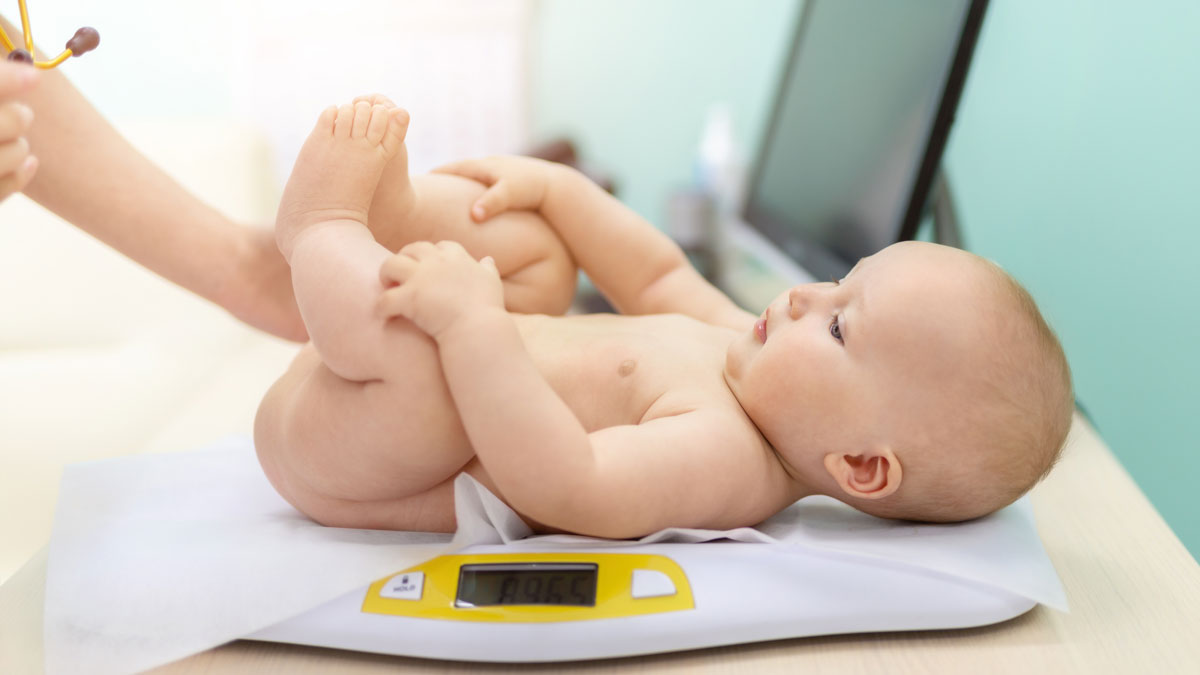 Pediatrician specialist taking measurement infant child weight during screening examination. Cute caucasian baby lying on electronic scales doctors office. Children healthcare and disease prevention